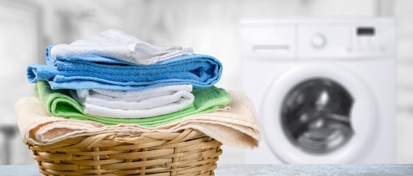 Wicker basket filled with colorful folded towels in front of white washing machine