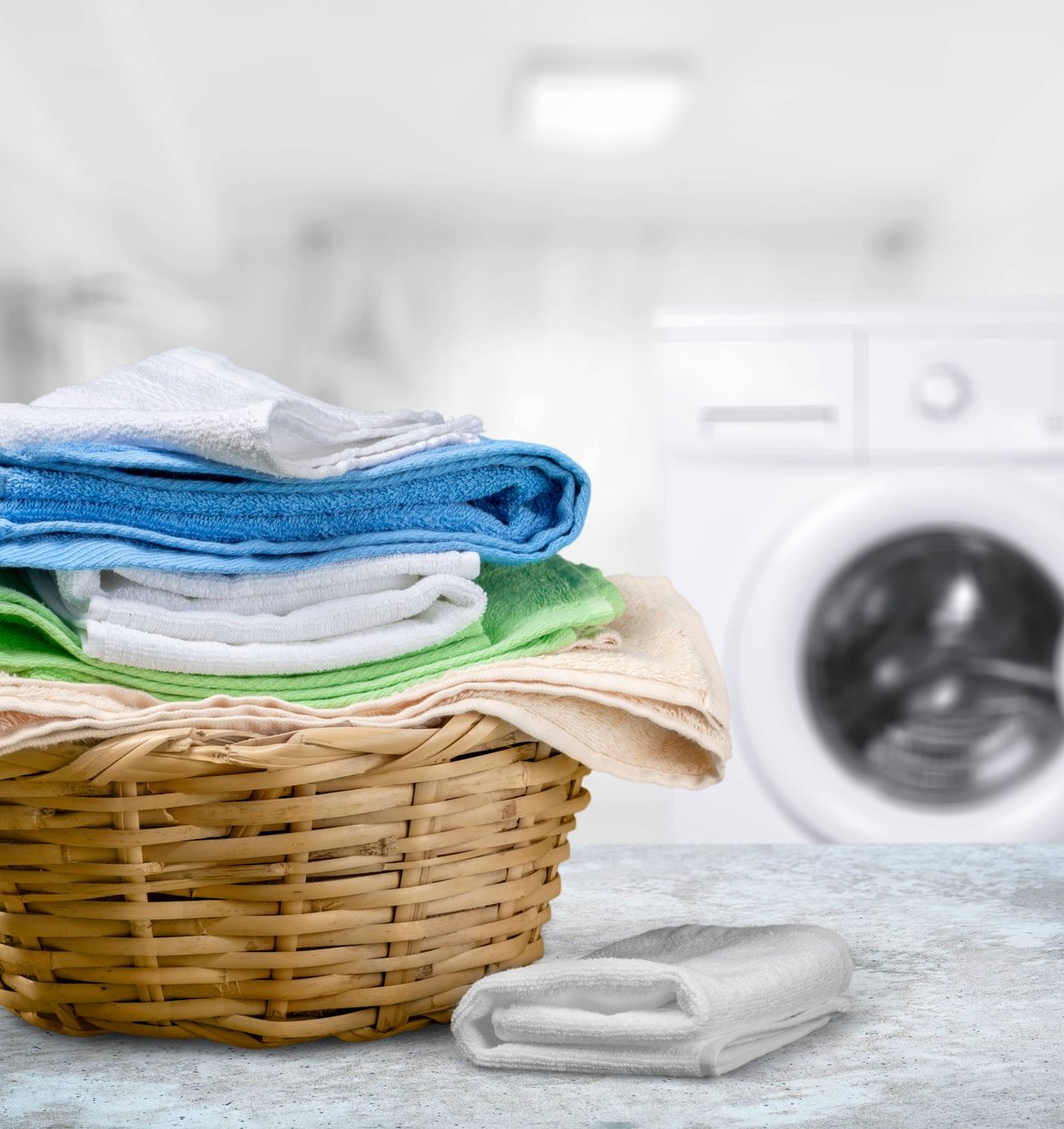 Worker in apron folding white linens at commercial laundry facility with washers