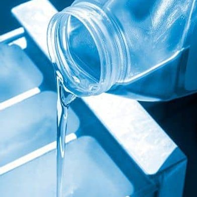 Clear water pouring from plastic bottle into glass container on blue surface