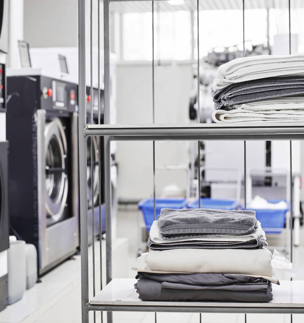 Worker in apron folding white linens at commercial laundry facility with washers